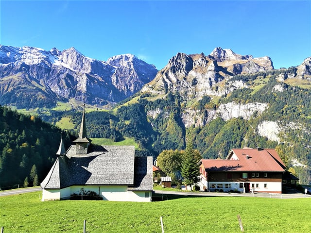 Eine Kapelle, dahinter die Alpengipfel bei strahlendem Sonnenschein.