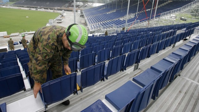 Ein Angehöriger der Schweizer Armee setzt Stühle auf eine Tribüne. Ein Angehöriger der Schweizer Armee setzt Stühle auf eine Tribüne.