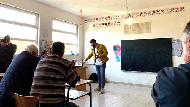 Bauern von Anë Vjosë in einer Schule. Vorne steht ein Redner der Investoren. Bauern von Anë Vjosë in einer Schule. Vorne steht ein Redner der Investoren.