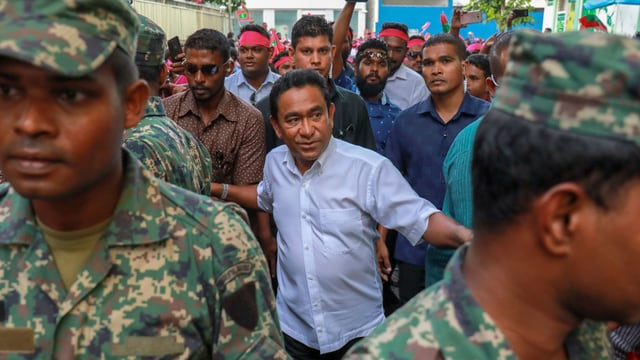 Yameen im Hemd umringt von Soldaten-Leibwächtern. Yameen im Hemd umringt von Soldaten-Leibwächtern.