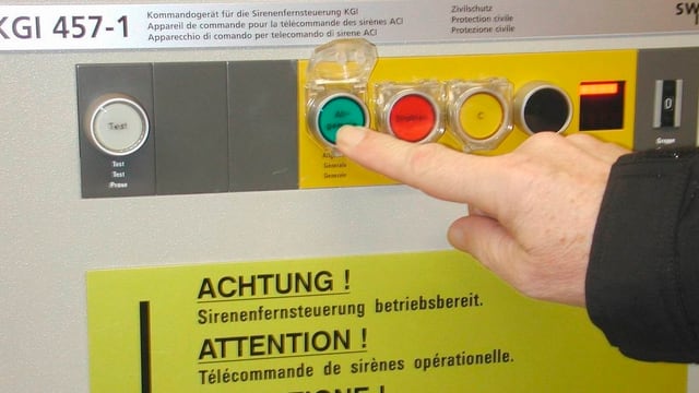 Ein Finger drückt den Knopf für den Sirenenalarm auf einer Schaltanlage. Ein Finger drückt den Knopf für den Sirenenalarm auf einer Schaltanlage.