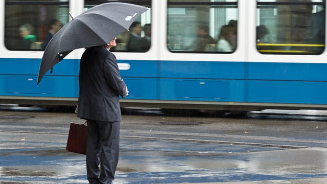 Mann in Anzug und mit Aktentasche und offenem Regenschirm vor einem Zürcher Tram. Mann in Anzug und mit Aktentasche und offenem Regenschirm vor einem Zürcher Tram.