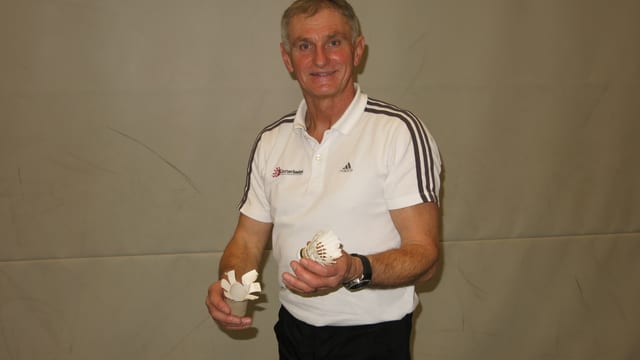 Hansjörg Thommen steht vor einer Wand. In der einen Hand hält er einen Federball, in der anderen eine WC Rolle. Hansjörg Thommen steht vor einer Wand. In der einen Hand hält er einen Federball, in der anderen eine WC Rolle.