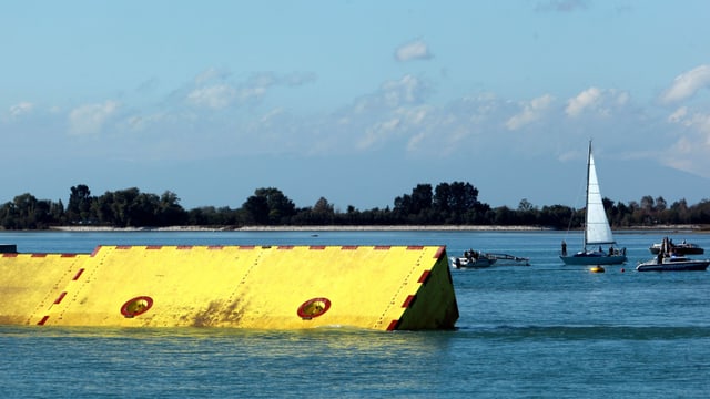 Gelbe Sperrelemente im Wasser neben Vergnügungsbooten.