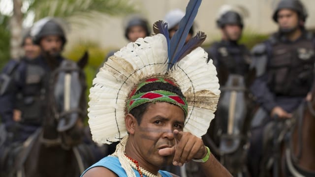 Ein Indo mit Kopfschmuck vor einer Reihe Polizisten mit Helmen auf Pferden. Ein Indo mit Kopfschmuck vor einer Reihe Polizisten mit Helmen auf Pferden.