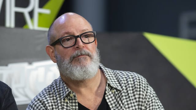 Mike Mignola, mit grauem Bart und markanter Brille, schaut nachdenklich ins Publikum Mike Mignola, mit grauem Bart und markanter Brille, schaut nachdenklich ins Publikum