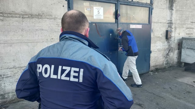 Mann öffnet Türschloss, Polizist schaut zu. Mann öffnet Türschloss, Polizist schaut zu.