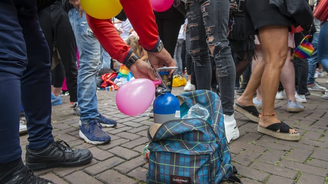 Eine Person füllt einen Ballon aus einer kleinen Gasflasche in einem Rucksack am Boden. Eine Person füllt einen Ballon aus einer kleinen Gasflasche in einem Rucksack am Boden.