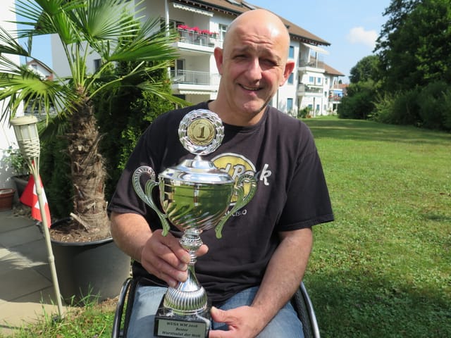Mann hält Pokal in der Hand. Wohnhäuser im Hintergrund. Mann hält Pokal in der Hand. Wohnhäuser im Hintergrund.