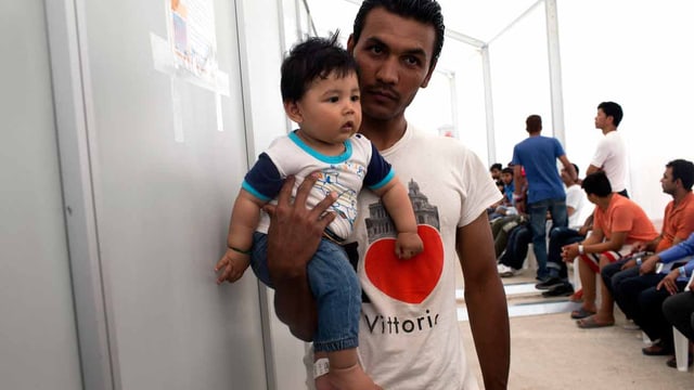 Ein Mann wartet in Griechenland im Aufnahmezentrum mit seinem Baby. Ein Mann wartet in Griechenland im Aufnahmezentrum mit seinem Baby.