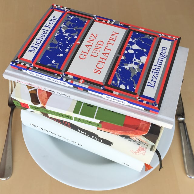 Es liegen fünf Bücher aufeinandergestappelt auf einem weissen Teller. Das Besteckt liegt daneben. Es liegen fünf Bücher aufeinandergestappelt auf einem weissen Teller. Das Besteckt liegt daneben.