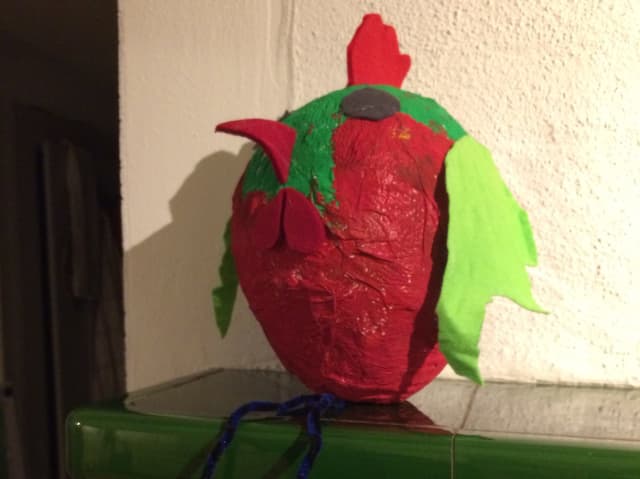 Rotes Huhn aus Pappmaché mit grünen Flügeln.