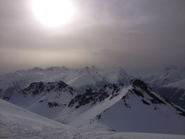 Verschneite Berggipfel sind zu sehen. Darüber scheint die Sonne nur milchig mit den vielen Aerosolen in der Luft. Verschneite Berggipfel sind zu sehen. Darüber scheint die Sonne nur milchig mit den vielen Aerosolen in der Luft.