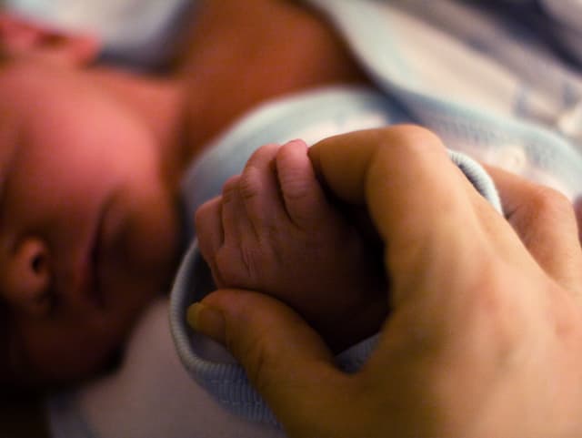 Die Hand eines Erwachsenen hält die Hand eines Neugeborenen.