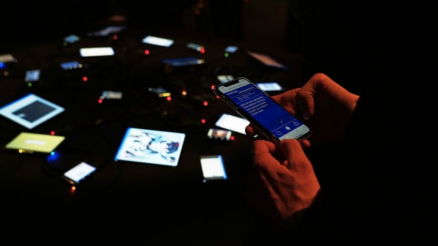 Einblick in eine Installation, in der viele kleine Bildschirme in einem dunklen Raum bläulich aufleuchten Einblick in eine Installation, in der viele kleine Bildschirme in einem dunklen Raum bläulich aufleuchten