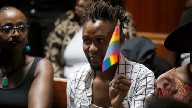 Männer und Frauen, einer hält ein Regenbogenfähnchen in die Luft. Männer und Frauen, einer hält ein Regenbogenfähnchen in die Luft.