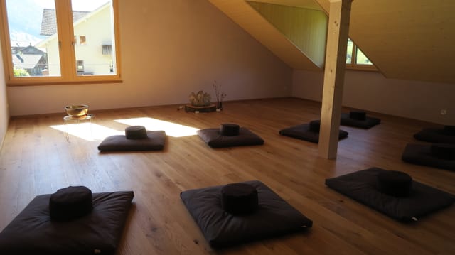 Blick in den Raum der Stille. Am Boden liegen Kissen, auf einem Sockel liegt ein grosser Kristall. Blick in den Raum der Stille. Am Boden liegen Kissen, auf einem Sockel liegt ein grosser Kristall.