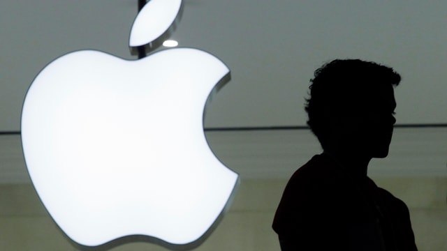 Ein Logo von Apple und der Schatten einer Person daneben. Ein Logo von Apple und der Schatten einer Person daneben.