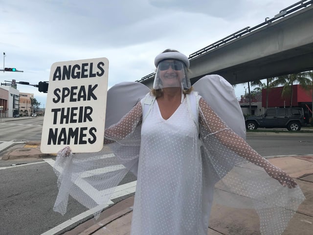 Frau in Engelskostüm und Schild "Engel sagen ihre Namen"