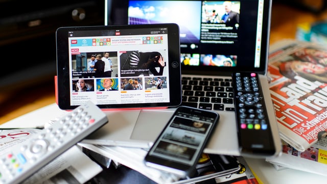 Ein Tisch mit Fernbedienungen, Handys, Laptops und Zeitschriften darauf. Ein Tisch mit Fernbedienungen, Handys, Laptops und Zeitschriften darauf.