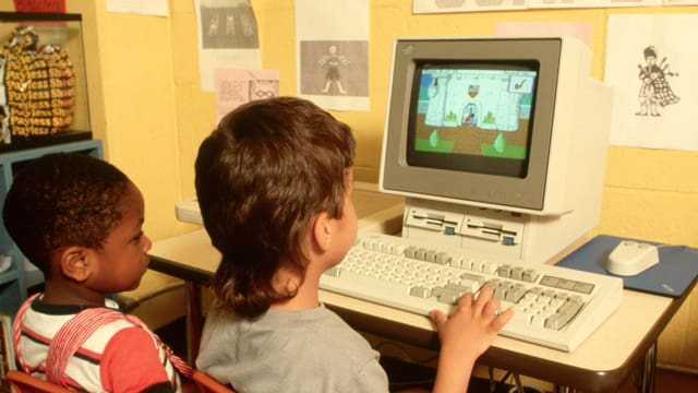 Bild von ca. 1990: Zwei Kinder sitzen vor einem altmodischen Computer, auf dem ein Spiel läuft Bild von ca. 1990: Zwei Kinder sitzen vor einem altmodischen Computer, auf dem ein Spiel läuft