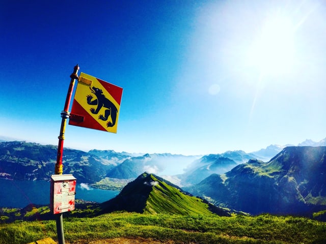 Blick vom Morgenberghorn/BE in die Talschaften vom Berner Oberland. Dazu blauer Himmel und im Vordergrund eine Fahne des Kantons Bern.
