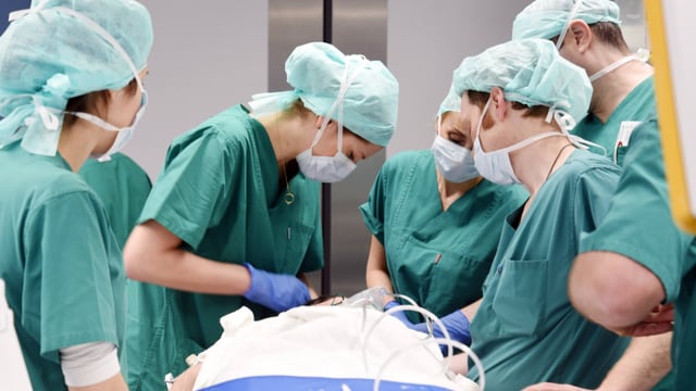 Symbolbild: Mehrere Personen in Operationsgewändern stehen um einen operierten Patienten. Symbolbild: Mehrere Personen in Operationsgewändern stehen um einen operierten Patienten.