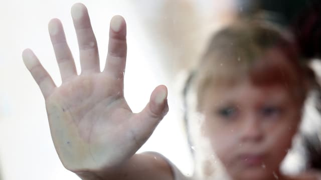 EIn kleines Mädchen hält die ausgestreckte flache Hand an eine Scheibe.