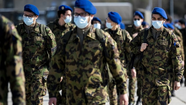 Soldaten mit Gesichtsschutz und blauen Berets in einer grossen Gruppe abgebildet. Soldaten mit Gesichtsschutz und blauen Berets in einer grossen Gruppe abgebildet.