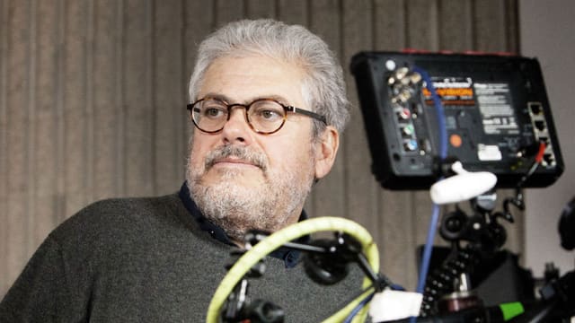 Roberto Andò mit Brille und schwarzen Pulli, neben einer Kamera. Roberto Andò mit Brille und schwarzen Pulli, neben einer Kamera.