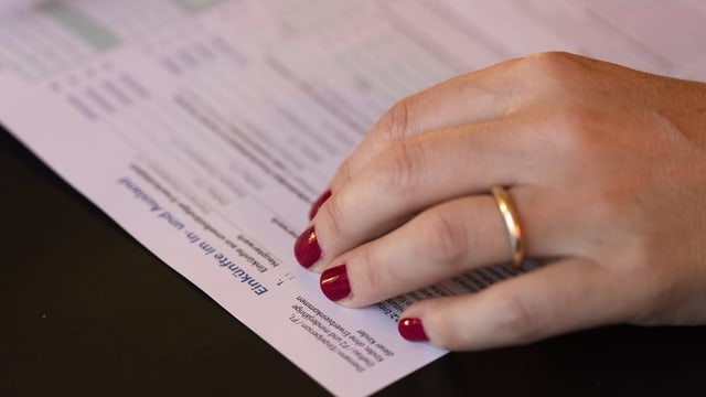 Eine Frau füllt eine Steuererklärung aus und trägt eineen Ehering. Eine Frau füllt eine Steuererklärung aus und trägt eineen Ehering.