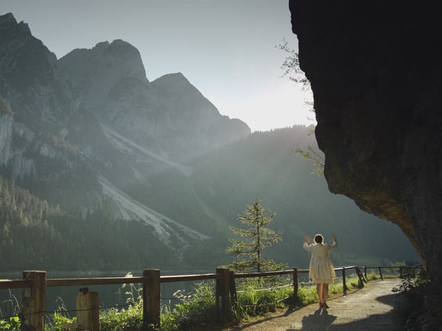 In einer Berglandschaft steht eine Frau an eine unsichtbare Wand gelehnt. In einer Berglandschaft steht eine Frau an eine unsichtbare Wand gelehnt.