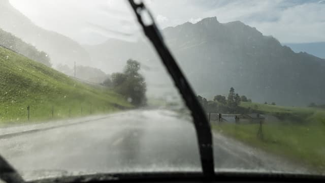 Blick durch Windschutzscheibe auf regenverhangene Berge. Blick durch Windschutzscheibe auf regenverhangene Berge.