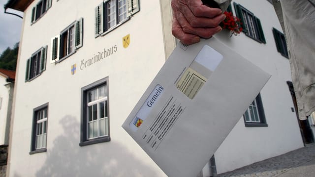 Ein Stimmbrechtigter mit Wahlcouvert vor dem Gemeindehaus. Ein Stimmbrechtigter mit Wahlcouvert vor dem Gemeindehaus.