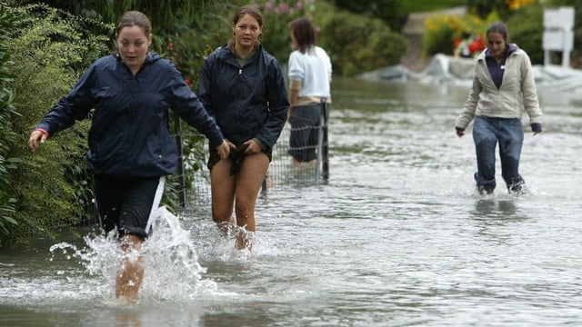 Menschen gehen auf einer überschwemmten Strasse.