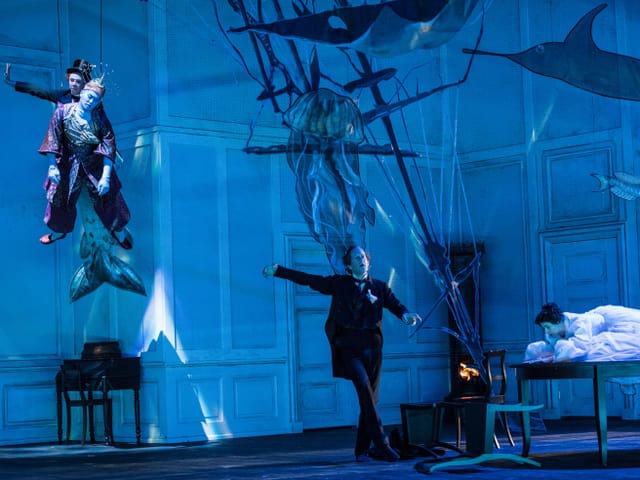 Bühne, auf welcher ein Schauspieler durch die Luft fliegt, ein weiterer auf der Bühne tanzt. Die Bühne ist in blaues Licht gehüllt und es wurde eine Art Unterwasserwelt kreiert. Bühne, auf welcher ein Schauspieler durch die Luft fliegt, ein weiterer auf der Bühne tanzt. Die Bühne ist in blaues Licht gehüllt und es wurde eine Art Unterwasserwelt kreiert.