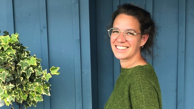 Eliane steht in vor einer blauen Wand und lächelt Eliane steht in vor einer blauen Wand und lächelt