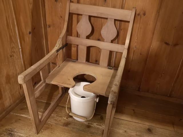 Stuhl aus Holz mit Loch in der Sitzfläche, darunter ein weisser Eimer. Stuhl aus Holz mit Loch in der Sitzfläche, darunter ein weisser Eimer.