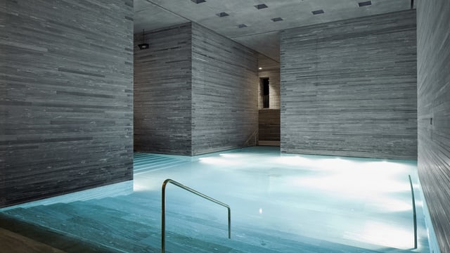 Schlichtes Thermalbad mit grauen Steinwänden und beleuchtetem Schwimmbecken Schlichtes Thermalbad mit grauen Steinwänden und beleuchtetem Schwimmbecken