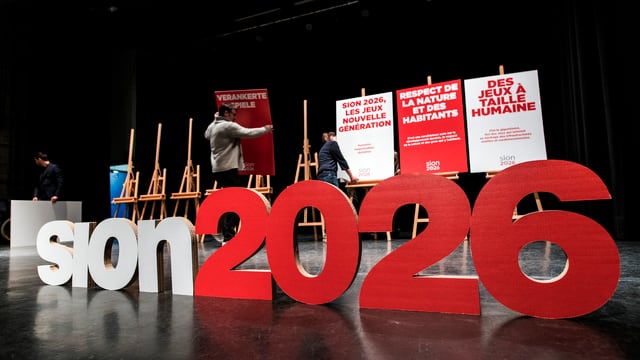 Logo von Sion 2026 auf einem Podium. Logo von Sion 2026 auf einem Podium.
