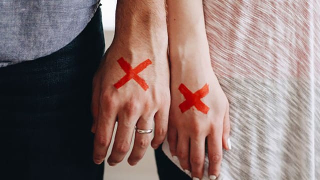 Eine Männerhand neben einer Frauenhand – beiden ist ein rotes X aufgemalt.