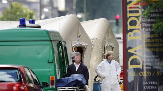 Ein Bestatter schiebt eine zugedeckte Leiche vom Tatort weg. Ein Bestatter schiebt eine zugedeckte Leiche vom Tatort weg.
