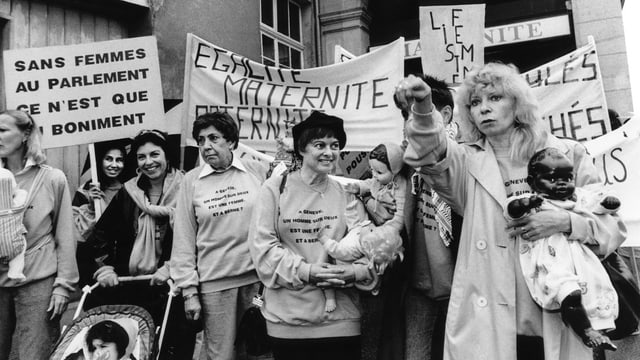 Brunner mit einer schwarzen Puppe im Arm inmitten von Demonstrantinnen, die mehr Frauen im Parlament fordern. Brunner mit einer schwarzen Puppe im Arm inmitten von Demonstrantinnen, die mehr Frauen im Parlament fordern.