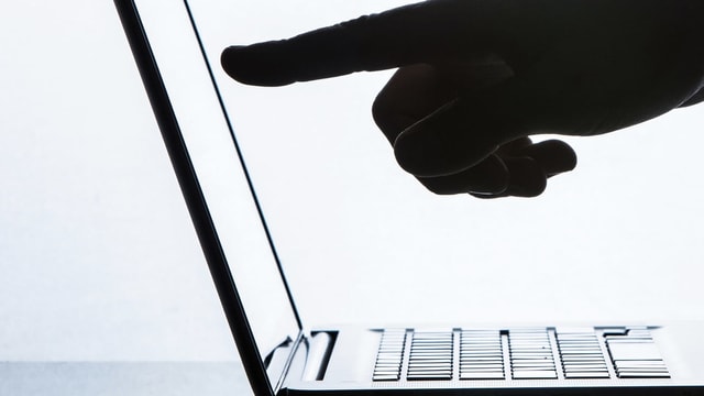 Ein Finger zeigt auf einen aufgeschlagenen Laptop. Ein Finger zeigt auf einen aufgeschlagenen Laptop.