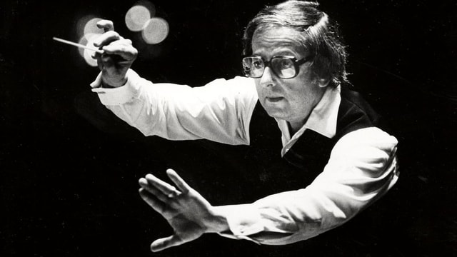 Ein Schwarz-Weiss-Bild von Andre Previn. Er hält einen Dirigentenstab. Ein Schwarz-Weiss-Bild von Andre Previn. Er hält einen Dirigentenstab.