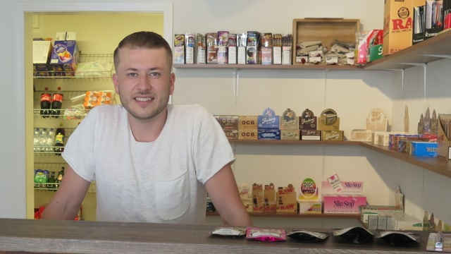 Ein CBD-Shop-Betreiber steht hinter der Theke seines Raucherwarenladens. Ein CBD-Shop-Betreiber steht hinter der Theke seines Raucherwarenladens.