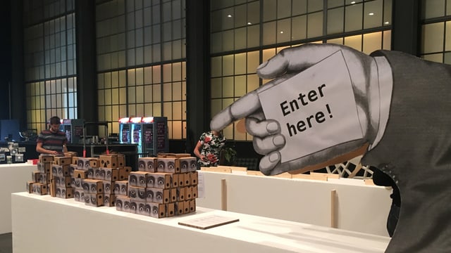 Ein Stapel von Google Cardboard-VR-Brillen und eine überdimensionierte Hand, die auf sie hinzeigt. Ein Stapel von Google Cardboard-VR-Brillen und eine überdimensionierte Hand, die auf sie hinzeigt.