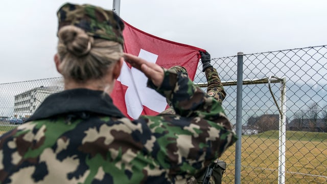 Soldatin salutiert vor Schweizer Flagge Soldatin salutiert vor Schweizer Flagge