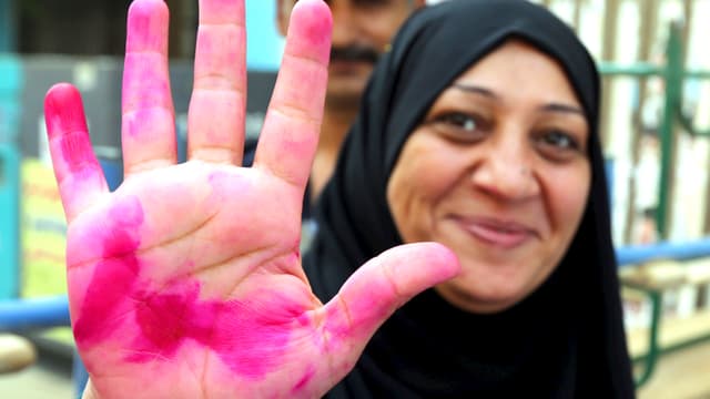 Eine ägyptische Hausfrau streckt ihre Handfläche in die Kamera und lacht. Die Hand ist rot von der Wahltinte. Eine ägyptische Hausfrau streckt ihre Handfläche in die Kamera und lacht. Die Hand ist rot von der Wahltinte.
