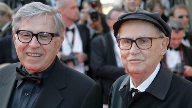 Zwei ältere Männer, beide mit Brille, man sieht sie ab den Schultern aufwärts. Sie tragen Anzüge und lächeln. Im Hintergrund verschwommen Fotografen. Zwei ältere Männer, beide mit Brille, man sieht sie ab den Schultern aufwärts. Sie tragen Anzüge und lächeln. Im Hintergrund verschwommen Fotografen.